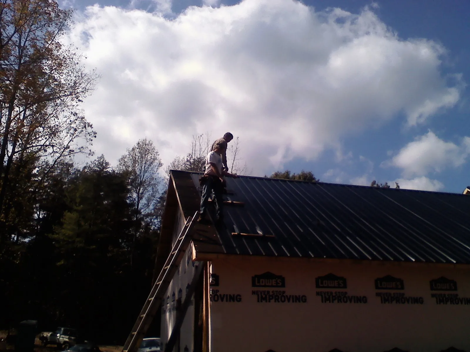 Roofer fastening dark metal panels high against a cloudy sky, from a Roof Inspection job in Zarephath