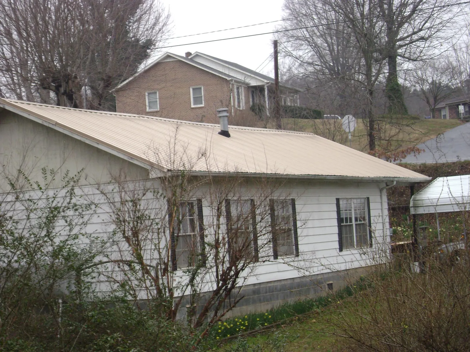 Tan metal roof on a white sided house set into a hillside — Commercial Roofing by Roofing Brothers in Zarephath